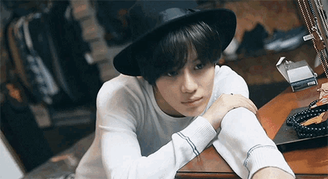 a young man wearing a hat and a white sweater is laying on a table .
