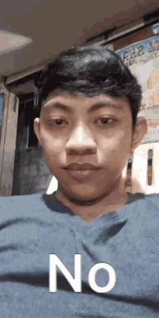a young man in a blue shirt is making a funny face with the word no on his face .