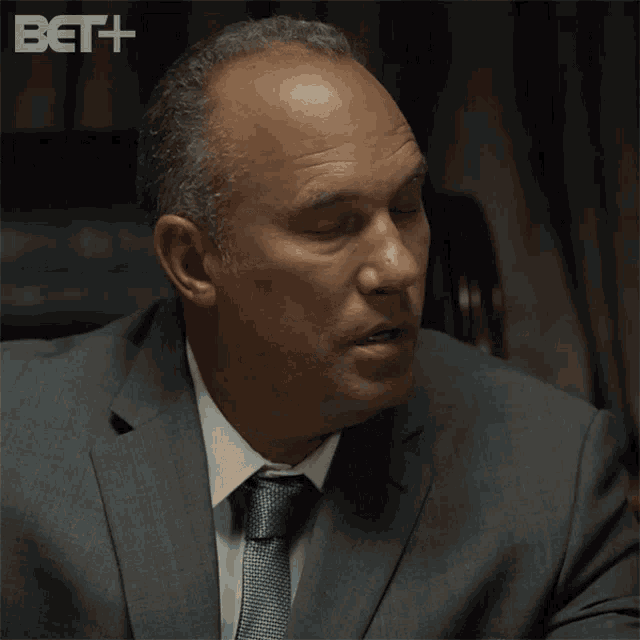 a man in a suit and tie is sitting in front of a bet advertisement