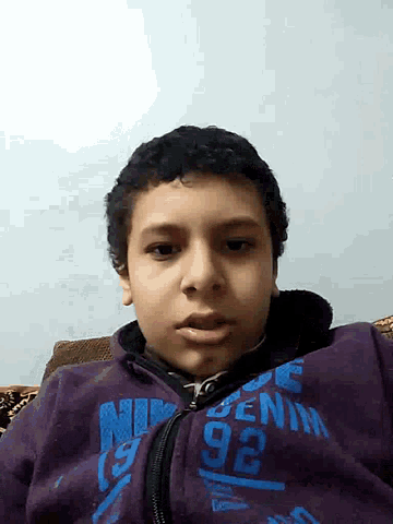 a young boy wearing a purple nike sweatshirt looks at the camera