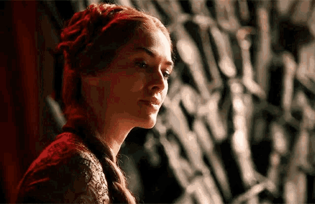 a woman with red hair is standing in front of a throne and looking at something .