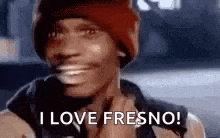 a man wearing a red beanie is smiling and says `` i love fresno '' .