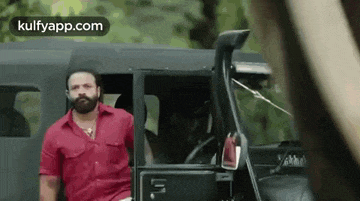a man in a red shirt is standing in front of a black jeep .