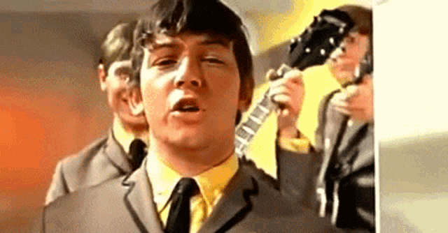 a man in a suit and tie is holding a guitar while singing .