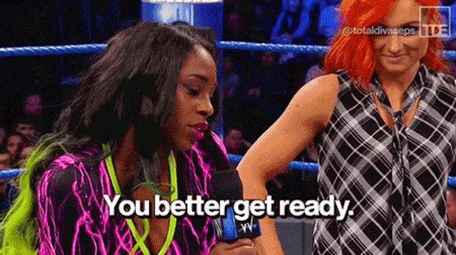 two women are standing in a wrestling ring talking into a microphone .