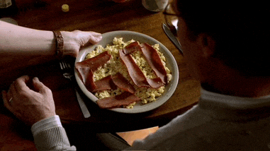 a man is sitting at a table with a plate of food with bacon and eggs on it
