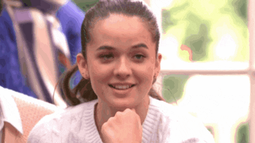a girl in a white sweater is smiling with her hand on her chin
