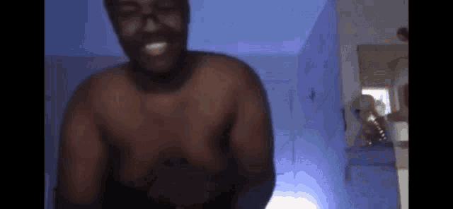 a man without a shirt is standing in a dark room and smiling .