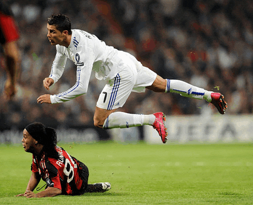 a soccer player with the number 7 on his jersey is flying over a player with the number 9 on his jersey