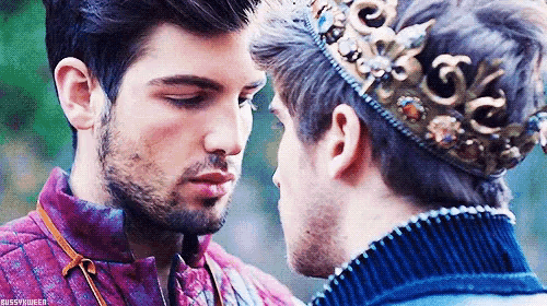 a man with a crown on his head is kissing another man .