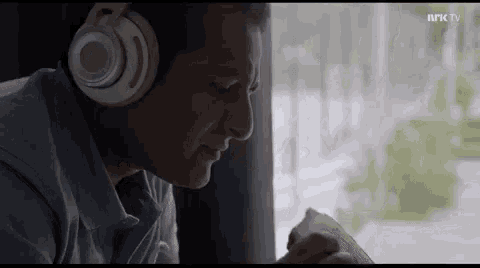 a man wearing headphones is sitting in front of a window and eating a sandwich .
