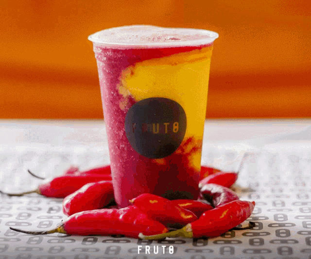 a cup of fruito sits on a table next to red peppers