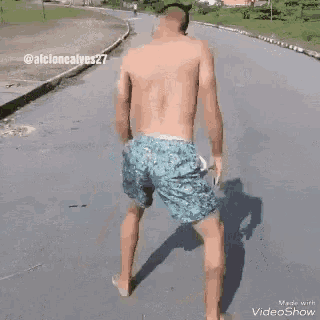 a shirtless man in blue shorts is dancing on a street .