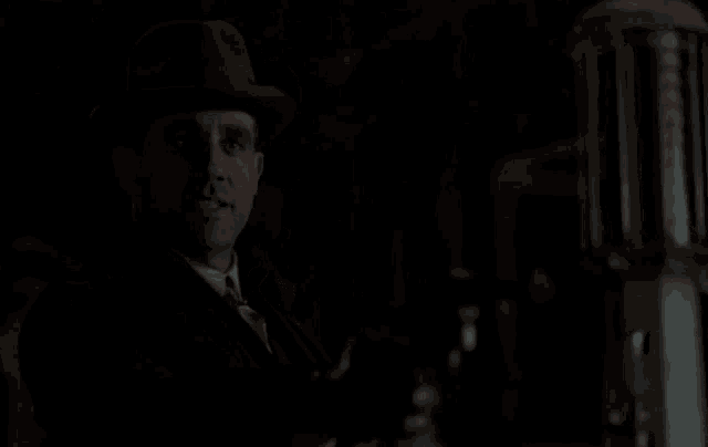 a man in a hat and tie is holding a camera in his hand in the dark .