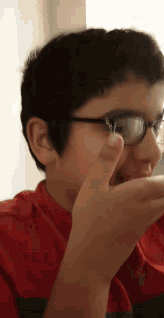 a young boy wearing glasses and a red shirt is covering his mouth