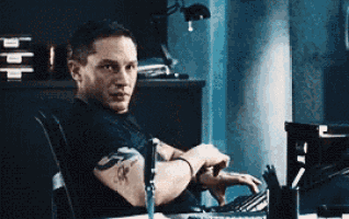 a man is sitting at a desk with a tattoo on his arm .