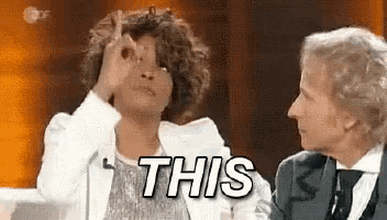 two women are sitting next to each other and one of them is making a gesture with her hand .