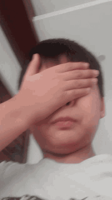 a boy covering his eyes with his hand