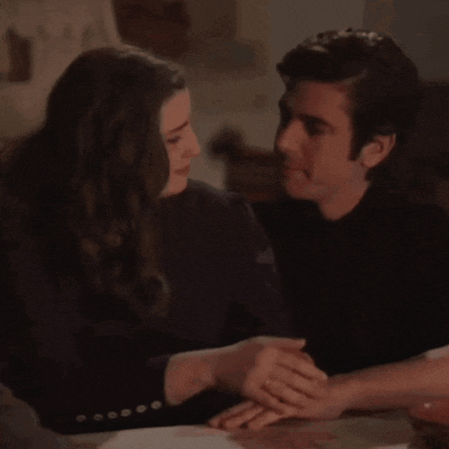 a man and a woman are holding hands and looking at each other while sitting at a table .
