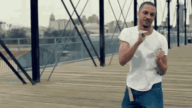 a man in a white t-shirt and blue jeans is standing on a bridge .