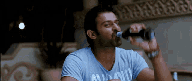 a man drinking from a bottle with a blue shirt that says all army