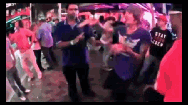 a group of people are dancing on a street with a man wearing a shirt that says stay true crew .