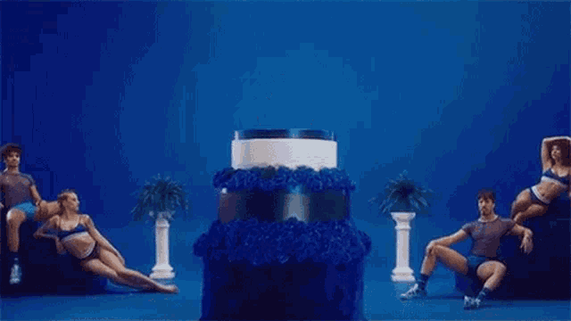 a woman is standing out of a cake surrounded by dancers .