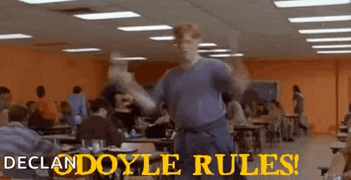 a man is dancing in a cafeteria with the words `` declan doyle rules '' written on the bottom .