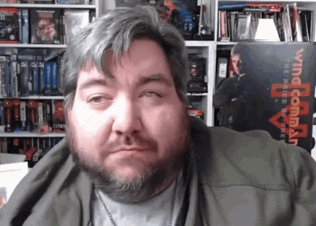 a man with a beard is sitting in front of a bookshelf with a box that says lying command