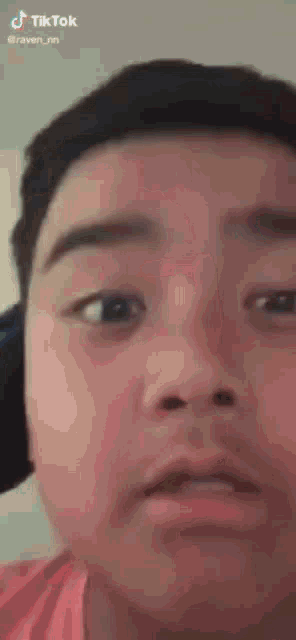 a close up of a young boy 's face with a pink shirt on .