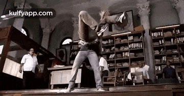 a man is doing a handstand in a library while another man looks on .