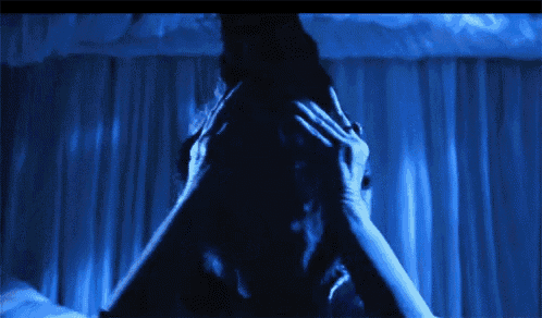 a woman is covering her face with her hands in a dark room