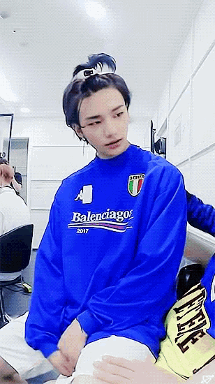 a boy wearing a blue balenciaga sweatshirt sits on a chair