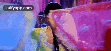 a woman in a yellow and pink dress is holding a pink cloth over her head .