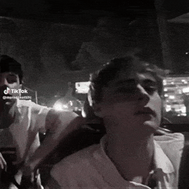a black and white photo of two young men sitting in a car at night .