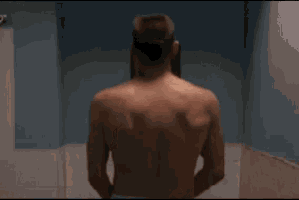 a man without a shirt is standing in a bathroom with his back to the camera .