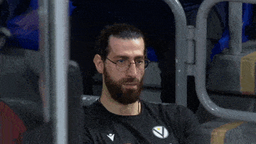 a man with glasses and a beard is wearing a black shirt with the letter v on the front