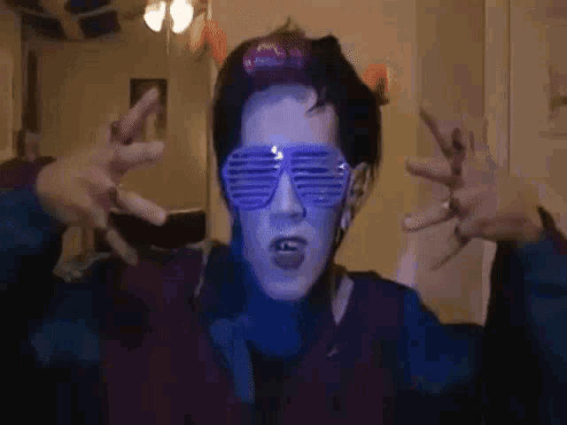 a person wearing purple sunglasses and a purple hat is making a peace sign