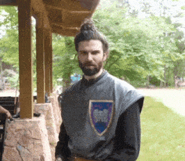 a man with a beard is wearing a gray vest with a blue shield on his chest