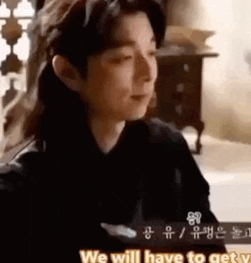 a man in a black shirt is sitting in a room talking to someone .