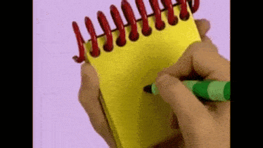 a person is writing on a yellow notebook with a green crayon .