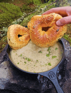 a person holding a bagel over a pot of soup