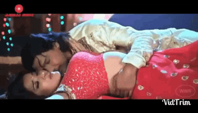 a man and a woman are kissing while laying on the floor . the woman is wearing a red saree .