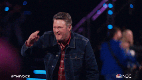 a man wearing a plaid shirt and a denim jacket is standing on a stage and waving