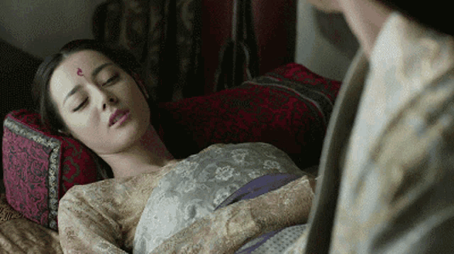 a woman is laying on a bed with a man standing next to her