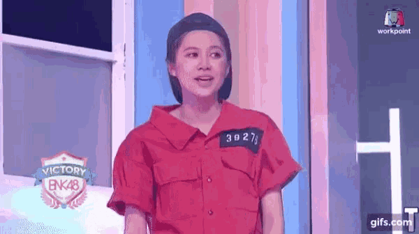 a woman wearing a red shirt and a hat is standing in front of a window .