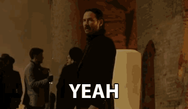 a man in a suit stands in front of a group of people and says " yeah "