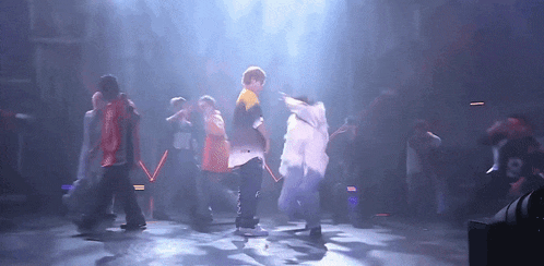 a group of people are dancing on a stage and one of them is wearing a shirt that says ' a ' on it