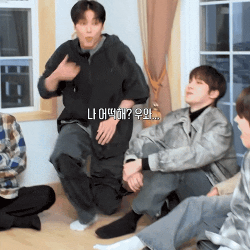 a group of young men are sitting on the floor and one of them is talking in korean