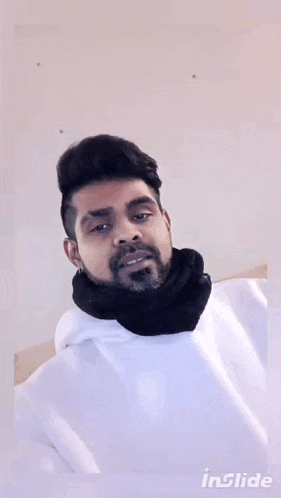 a man with a beard wearing a white hoodie and a black scarf around his neck